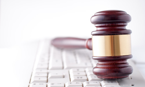 Conceptual image of a gavel used by a judge or auctioneer with a brass band around the head lying on a computer keyboard