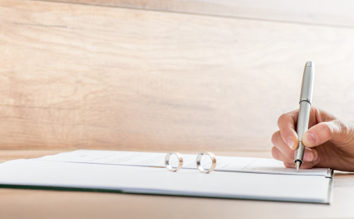 Closeup of female hand signing divorce papers with the two rings standing on the document.